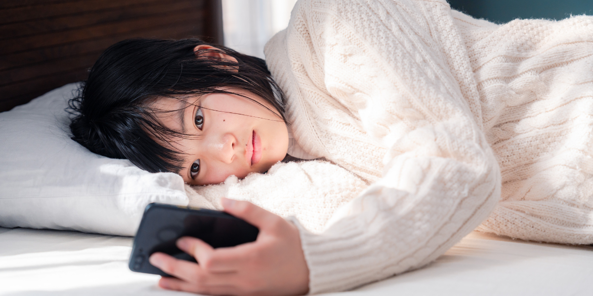ベッドでスマホを眺めている女性