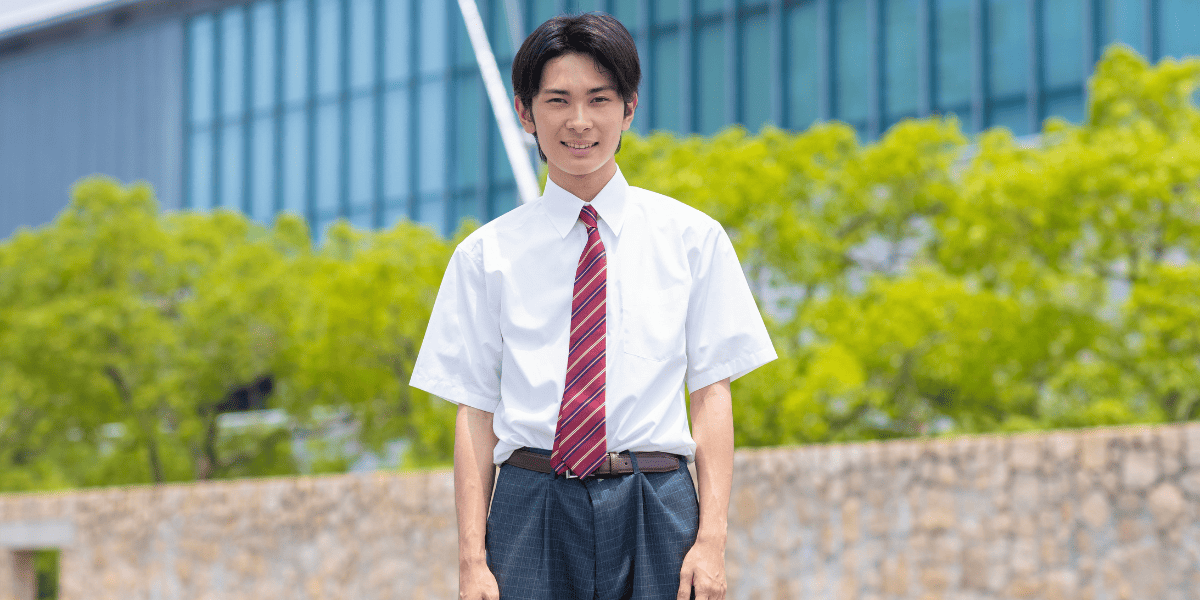 校舎を背景に立つ男子高校生