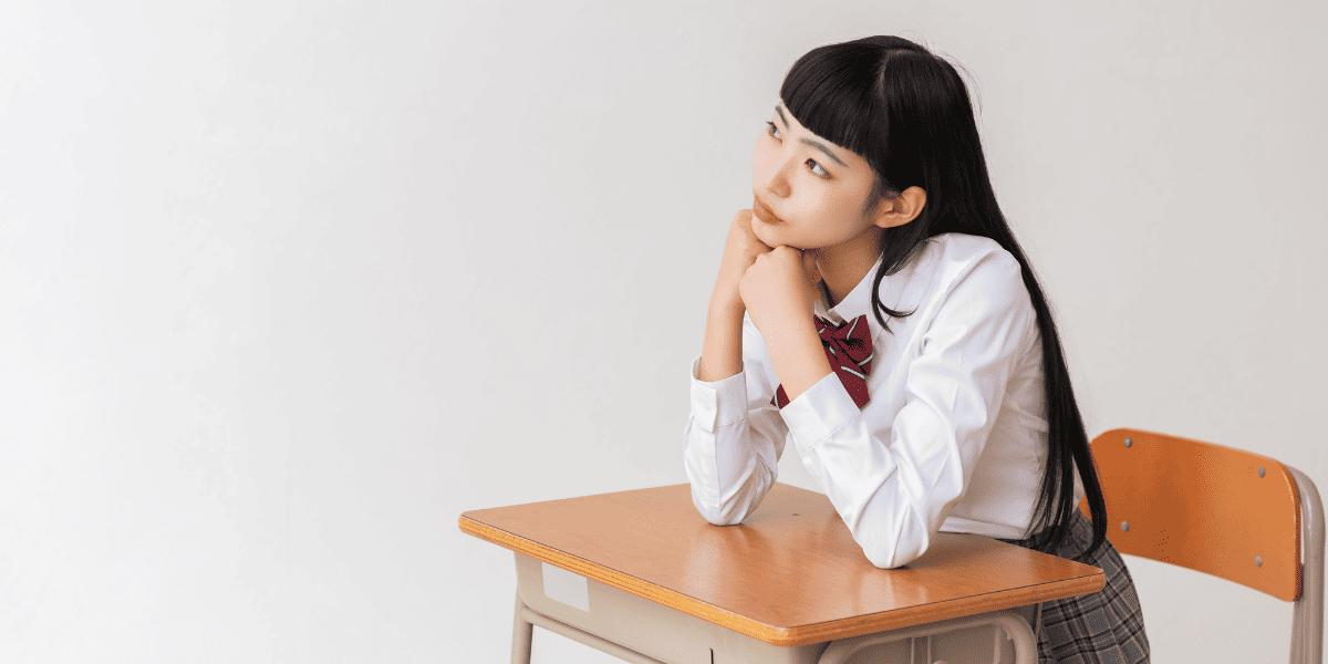 机に肘をついて考えている女子高校生