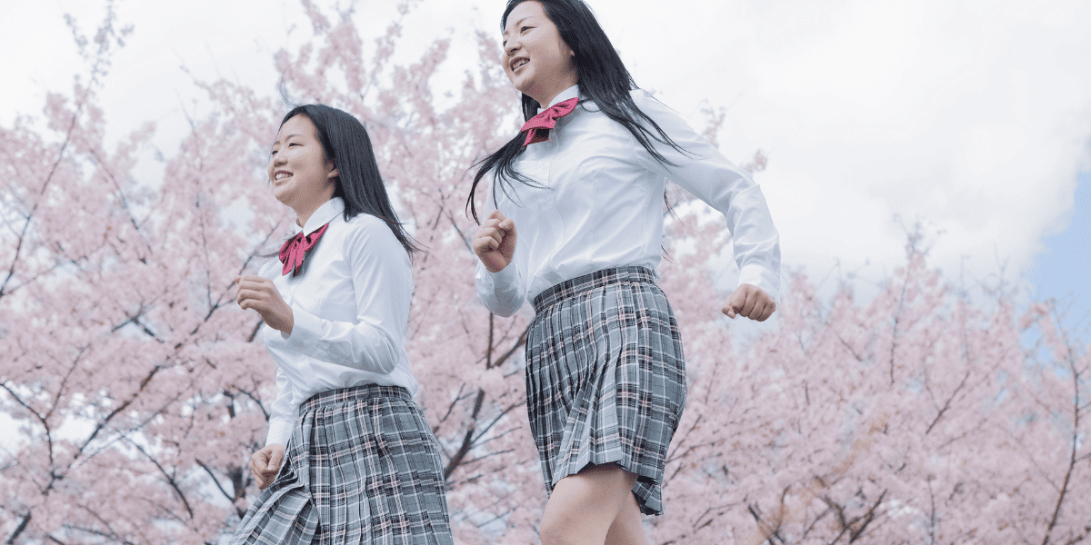 桜の木の下を走る女子生徒たち