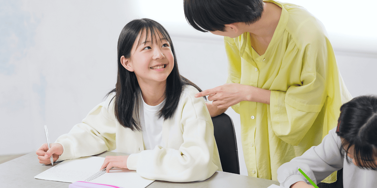 ノートをとる生徒と優しく話しかける先生