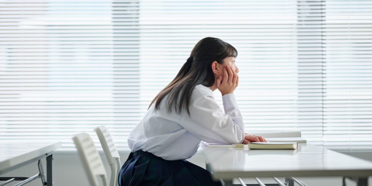 教室で頬杖をついている女子高校生